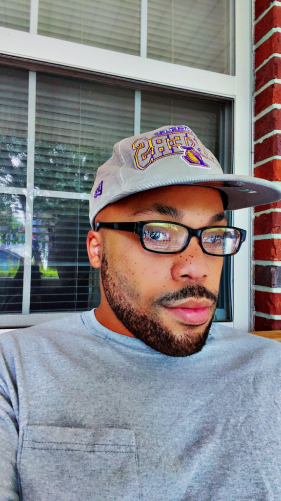 Black man wearing a grey hat, glasses, and grey shirt